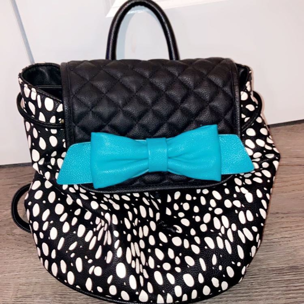 A Betsey Johnson hand bag purse/backpack. It is black/white with a teal bow.
